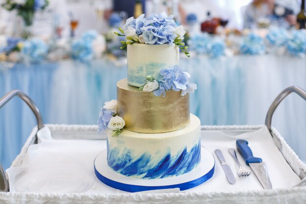 schöne Hochzeitstorte mit Blumen auf einem Tablett hautnah dekoriert. weiße und blaue abgestufte Hochzeitstorte mit einer Gabel und einem Messer