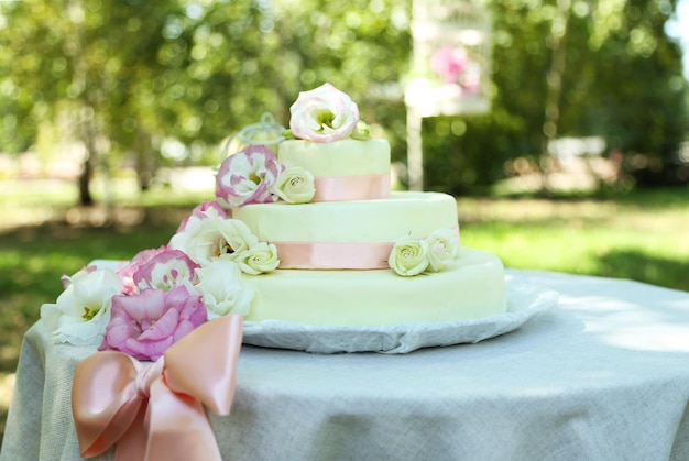 Foto schöne hochzeitstorte mit blumen auf tisch im freien