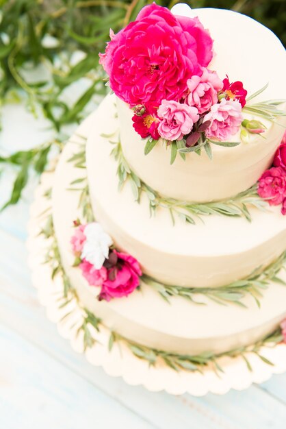 Schöne Hochzeitstorte mit Blumen, im Freien. Drei Ebenen