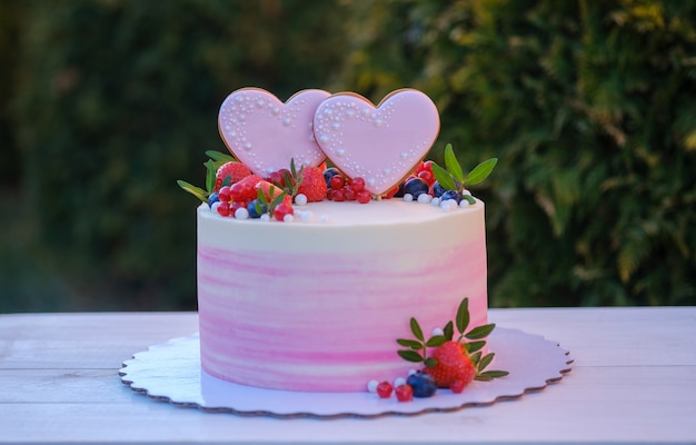 Schöne Hochzeitstorte mit zwei Herzen verziert mit frischen Erdbeeren, Johannisbeeren und Blaubeeren