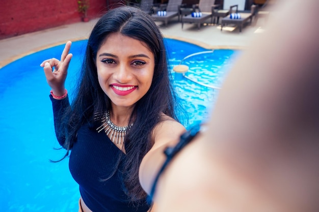 Schöne indische Frau mit weißem Lächeln Selfie-Porträt auf Smartphone-Kamera Sommercafé auf dem Seeweg am Swimmingpool Goa