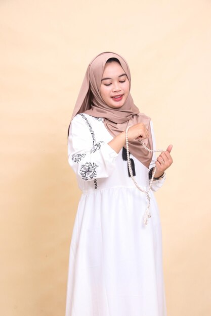 Schöne indonesische muslimische erwachsene Frau im Hijab hält Gebetsperlen in ihren Händen und lächelt offen.