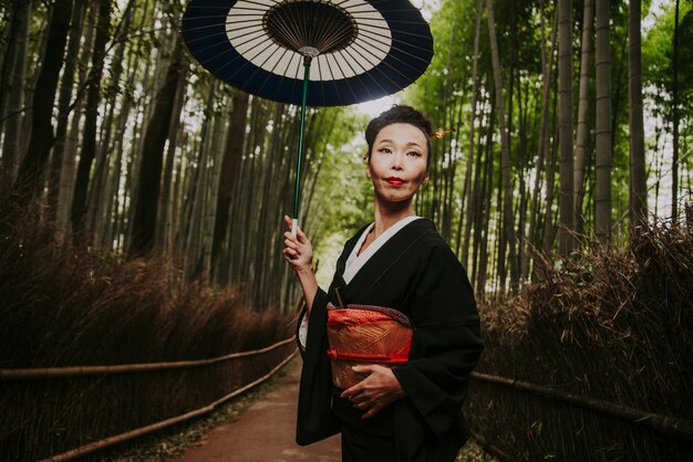 Foto schöne japanische ältere frau, die im bambuswald geht