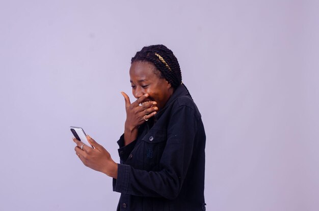 Schöne junge Afrikanerin, die ihr Telefon benutzt, erstaunt aussieht und sich freut