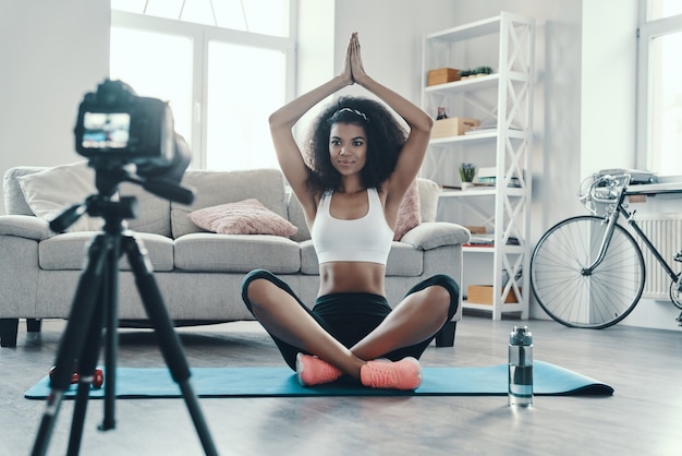 Schöne junge Afrikanerin, die im Yoga sitzt, während sie ein Social-Media-Video macht