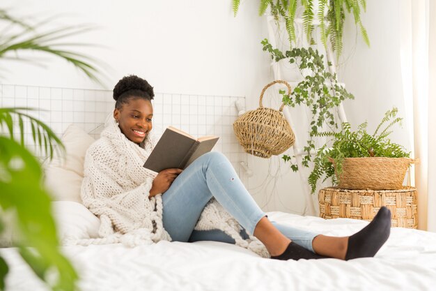 schöne junge afrikanische Frau, die auf Bett mit einem Buch sitzt