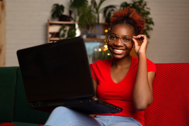 schöne junge afrikanische Frau, die mit einem Laptop auf der Couch sitzt