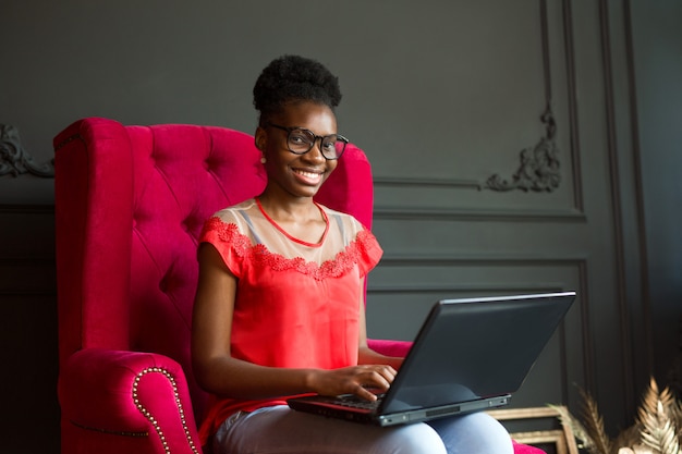 Schöne junge afrikanische Frau mit Laptop auf Sofa