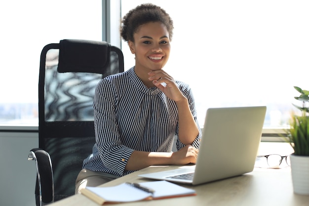 Schöne junge Afroamerikanerfrau sitzt im Büro und schaut in die Kamera.