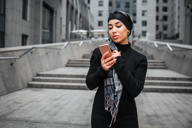 Schöne junge arabische Frau steht und schaut am Telefon.