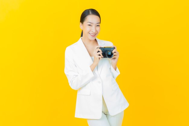Schöne junge asiatische Frau des Porträts benutzt Kamera auf Farbwand