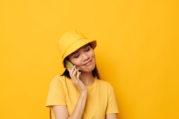 Schöne junge asiatische Frau des Porträts in einem gelben Hut und in einem T-Shirt, das am Telefon spricht Lebensstil unverändert