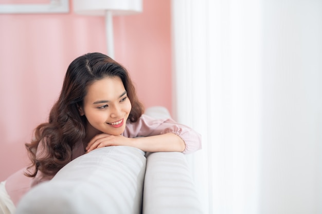 Schöne junge asiatische Frau, die auf Sofa entspannt.