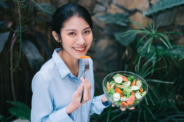 Schöne junge asiatische Frau, die Frühstück mit Salat genießt