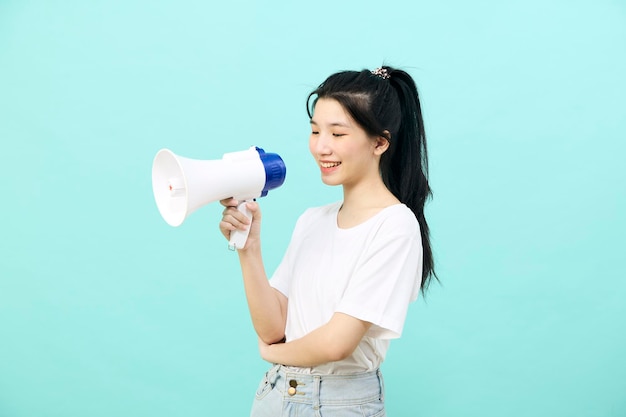 Schöne junge asiatische Frau, die Megaphon auf blauem Hintergrundstudio hält