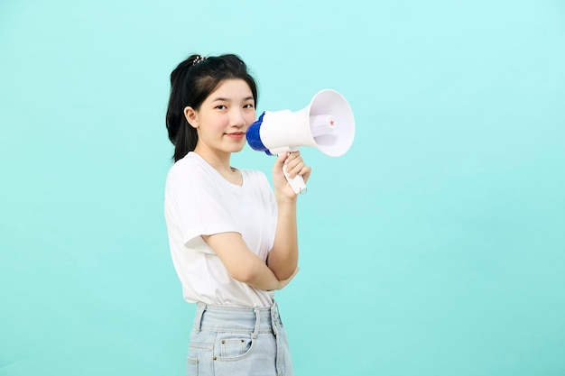 Schöne junge asiatische Frau, die Megaphon auf blauem Hintergrundstudio hält