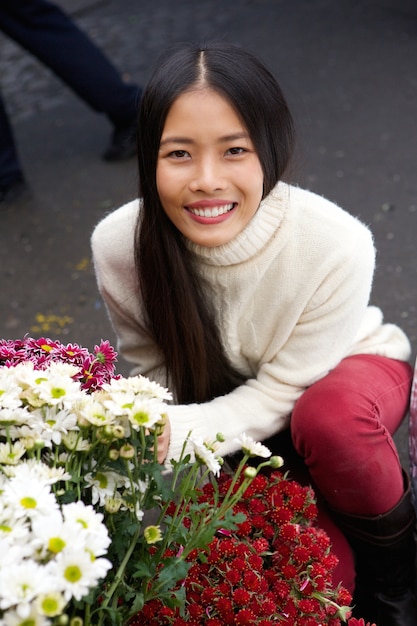 Schöne junge asiatische Frau, die mit Blumen am Geschäft lächelt