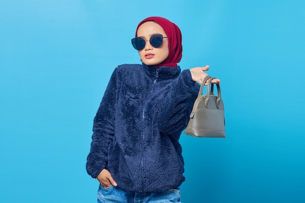 Schöne junge asiatische Frau, die Tasche mit einem glücklichen Ausdruck auf blauem Hintergrund hält