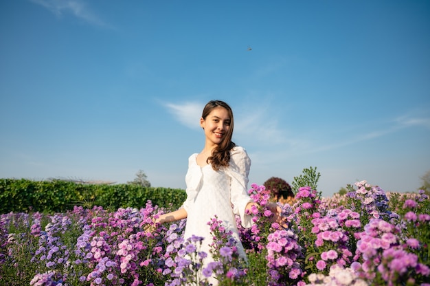 Schöne junge asiatische frau im weißen kleid, die margaretblume genießt, die im garten auf der sonnigen blüht