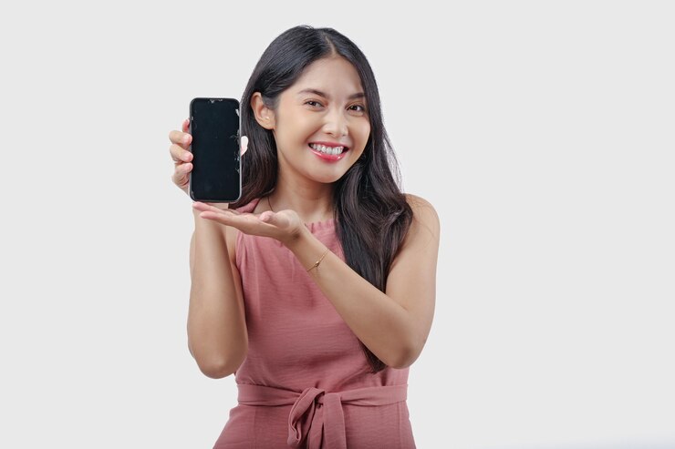 Schöne junge asiatische Frau in rosa Kleid zeigt den Kopierraum auf dem Telefonbildschirm