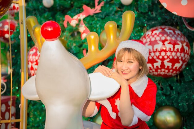 Schöne junge asiatische Frau in Weihnachtsmann-Kleidung im FreienThailänderGesendetes Glück für KinderFrohe WeihnachtenWillkommen im WinterDekorierter Weihnachtshintergrund