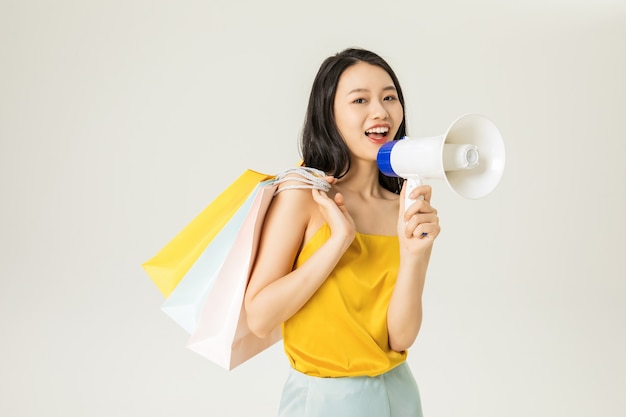 Schöne junge asiatische Frau mit Einkaufstüten und Lautsprechern isoliert