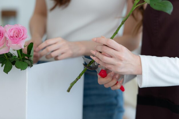 Schöne junge asiatische Frau schneidet in einem Blumenladen eine Rosenblume.