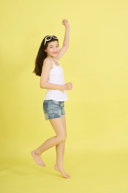 Schöne junge asiatische Frauen mit Sonnenbrille auf dem Kopf, die auf gelbem Hintergrund springen