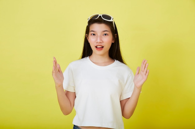 Schöne junge asiatische Frauen mit Sonnenbrille auf dem Kopf mit den Händen auf gelbem Hintergrund