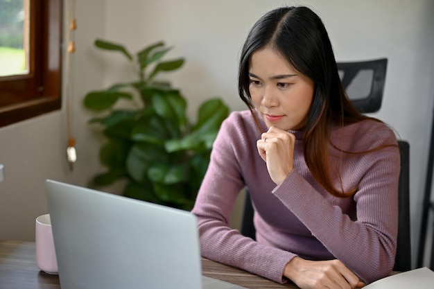 Schöne junge asiatische Mädchen mit Laptop, die auf den Laptop-Bildschirm schaut