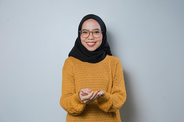 Schöne junge asiatische Muslimin mit orangefarbenem Pullover und Brille, die beide Hände ausstreckt