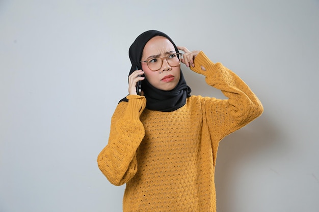 Schöne junge asiatische muslimische Frau trägt orangefarbenen Pullover und Brille, während sie ihr Mobiltelefon benutzt