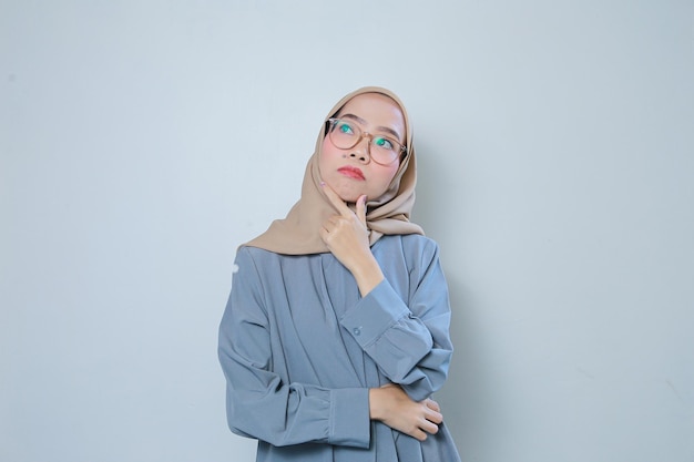 Schöne junge asiatische muslimische Geschäftsfrau denkt mit Brille vor isoliertem Hintergrund