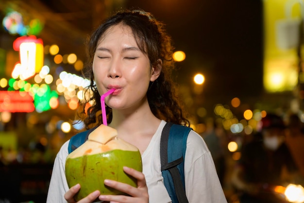Schöne junge asiatische Touristenfrau im Urlaub, die nachts die Khao San Road besichtigt und erkundet