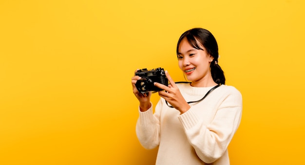 Schöne junge asiatische touristische Studioaufnahme mit der Kamera in der Hand isoliert auf gelbem Hintergrund.