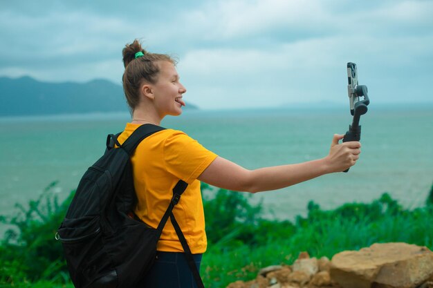 Schöne junge Bloggerin im Freien, die wandert, reist, wandert, hält einen Stabilisator oder Gimbal mit