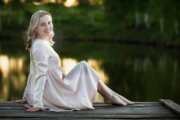 Schöne junge blonde Frau auf einer Holzbrücke in der Nähe des Flusses posiert mit Blick auf die Kamera