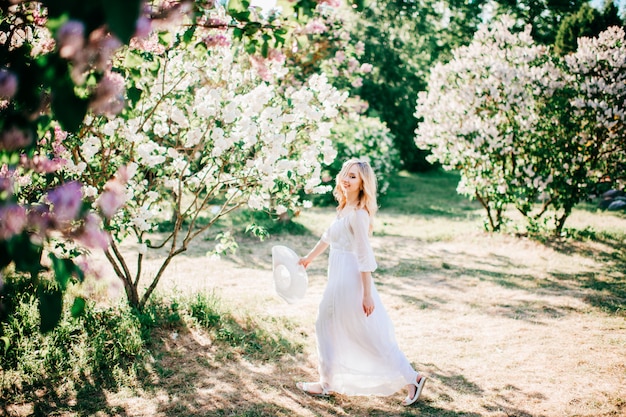 Schöne junge blonde Frau im weißen Kleid, das im sonnigen Sommerpark aufwirft.