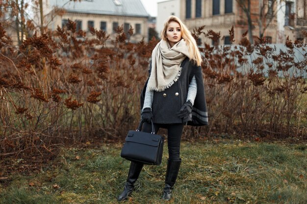 Schöne junge blonde Frau in einem stilvollen Herbstmantel mit einer schwarzen Handtaschenmode