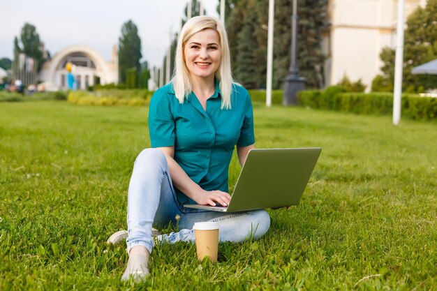 Schöne junge blonde Frau mit einem Laptop im Park an einem warmen Sommertag