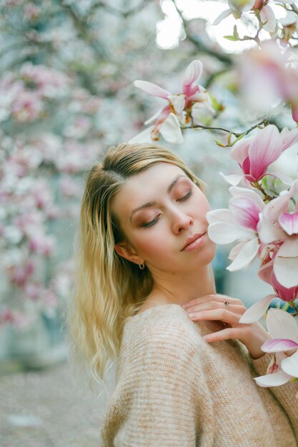 Schöne junge Blondine nahe einem blühenden Magnolienbaum