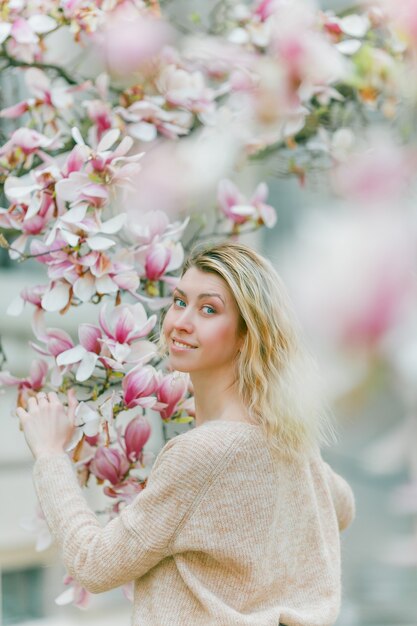 Schöne junge Blondine nahe einem blühenden Magnolienbaum