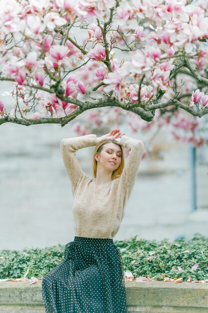 Schöne junge Blondine nahe einem blühenden Magnolienbaum