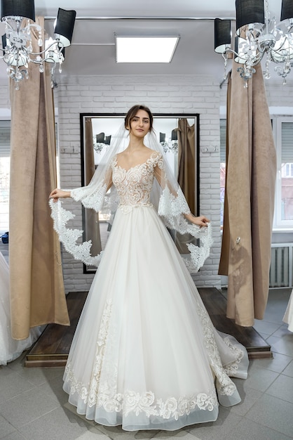 Schöne junge Braut, die im Hochzeitskleid im Salon aufwirft