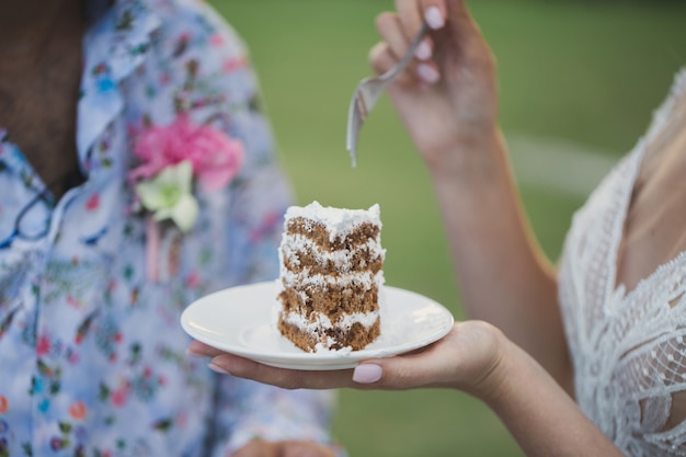 Schöne junge Braut füttert Hochzeitstorte, um draußen zu pflegen