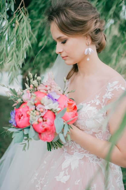 Schöne junge Braut im weißen Hochzeitskleid, das im Freien mit Blumenstrauß aufwirft