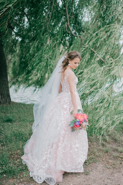 Schöne junge Braut im weißen Hochzeitskleid, das im Freien mit Blumenstrauß aufwirft