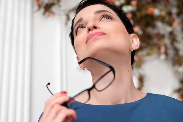 Schöne junge Brünette Frau hält Brille in der Hand und schaut auf