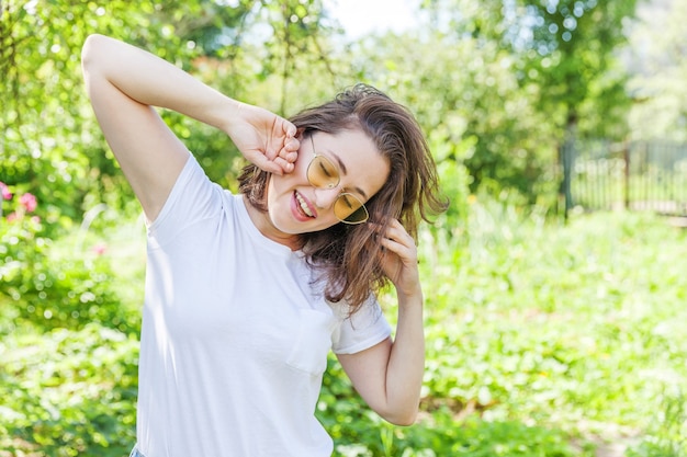 Schöne junge Brünette Frau mit braunen Haaren in der trendigen gelben Sonnenbrille, die auf Park- oder Gartengrün ruht und lächelt