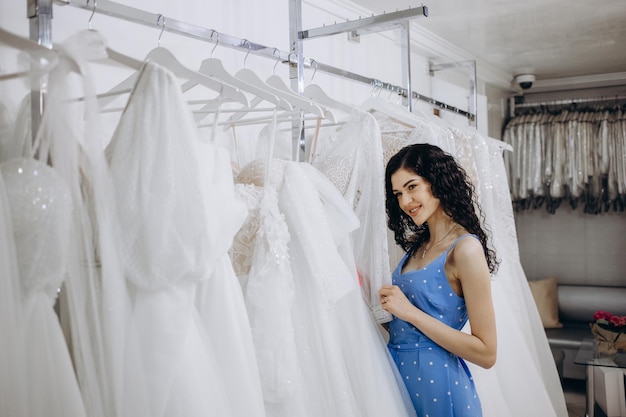 Schöne junge Brunettefrau, die Hochzeitskleid in einem Brautsalon wählt